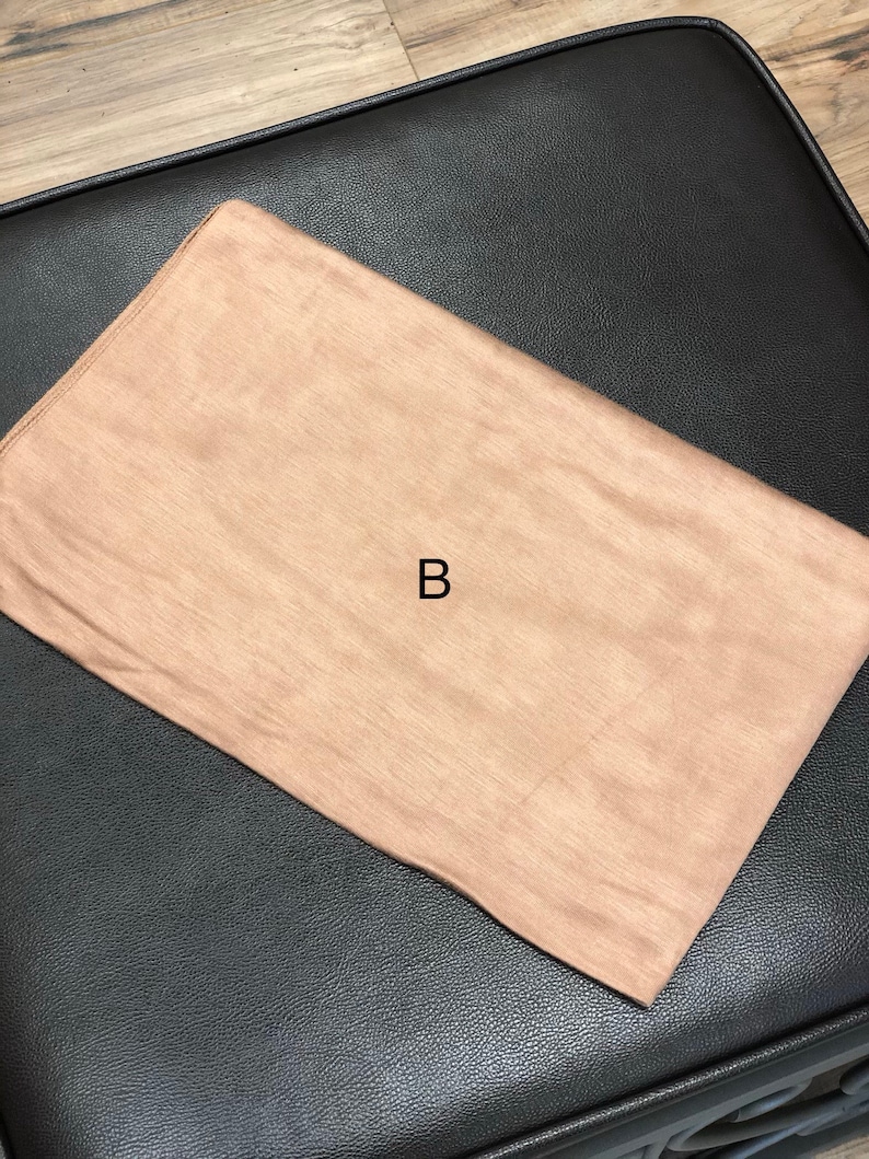 Puede incluir: Un rect&aacute;ngulo de tela marr&oacute;n claro con la letra "B" en el centro.