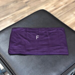 Puede incluir: Un rect&aacute;ngulo de tela morado con la letra "F" impresa en blanco en el centro.