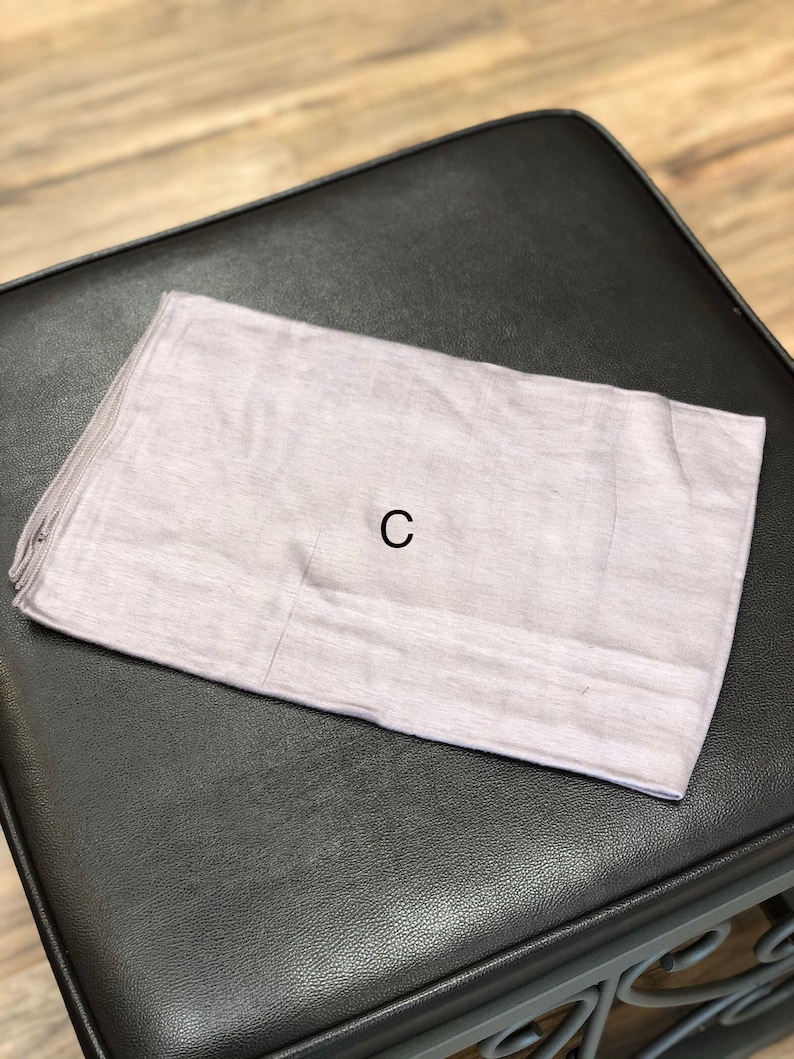 Puede incluir: Un rect&aacute;ngulo de tela gris claro con la letra "C" impresa en negro en el centro.