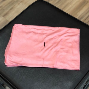 Puede incluir: Un rect&aacute;ngulo de tela suave de color melocot&oacute;n, posiblemente una bufanda o un chal, que se encuentra plano sobre una superficie negra.