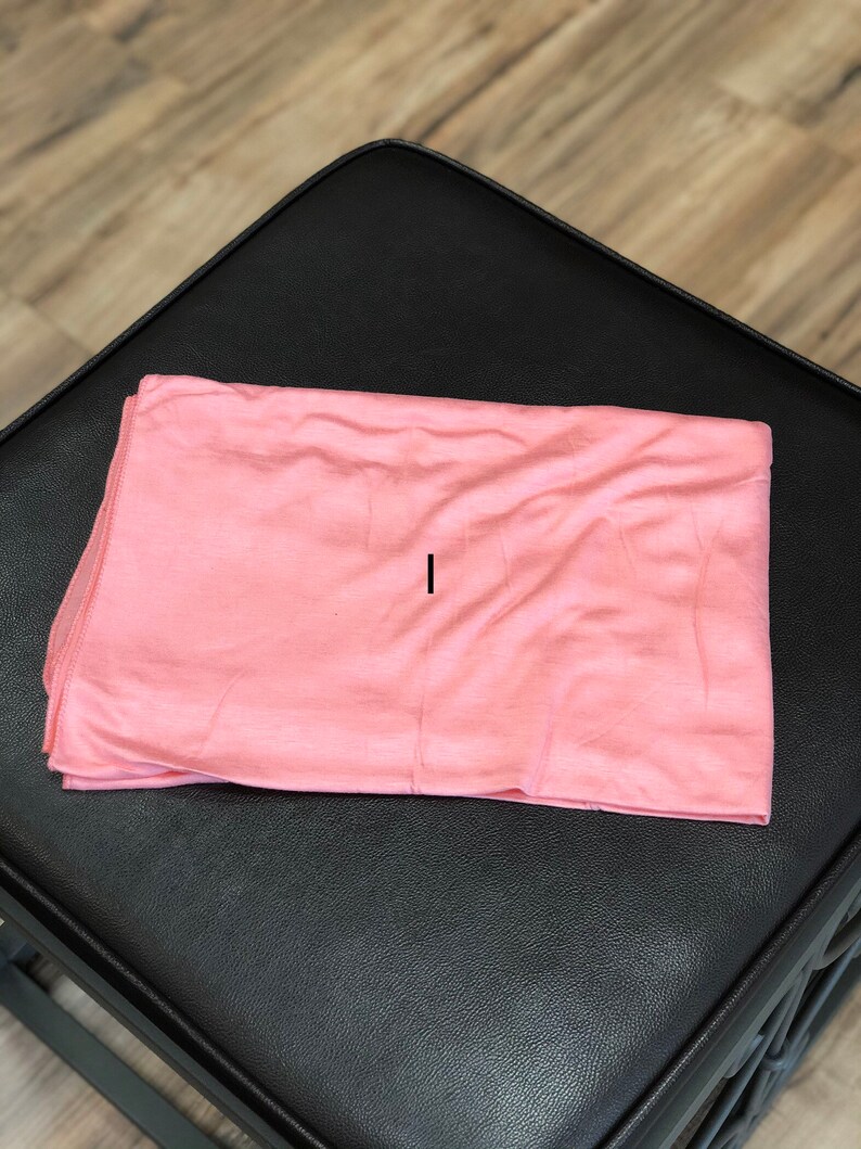 Puede incluir: Un rect&aacute;ngulo de tela suave de color melocot&oacute;n, posiblemente una bufanda o un chal, que se encuentra plano sobre una superficie negra.