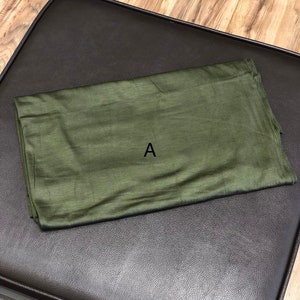 Puede incluir: Un trozo de tela verde doblado con la letra "A" impresa en &eacute;l.