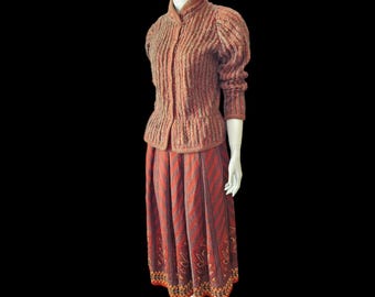 May include: A brown and beige knitted sweater with a high collar and long sleeves, paired with a red and brown patterned skirt. The skirt has a pleated design and a decorative trim.