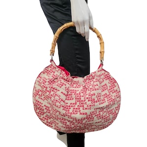 May include: A round handbag with a bamboo handle. The bag is cream-colored with a repeating red text pattern that reads "CHEAP AND CHIC". The interior is red.