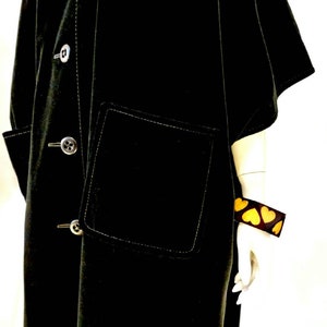 Puede incluir: Una chaqueta de terciopelo negro con cierre de botones, un gran bolsillo de parche y detalles de costura blanca. La chaqueta tiene un corte holgado y de gran tama&ntilde;o.