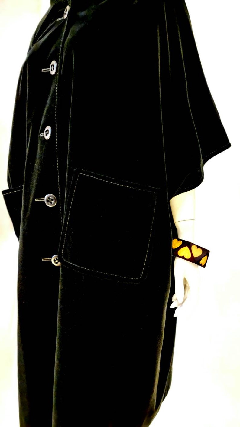 Puede incluir: Una chaqueta de terciopelo negro con cierre de botones, un gran bolsillo de parche y detalles de costura blanca. La chaqueta tiene un corte holgado y de gran tama&ntilde;o.