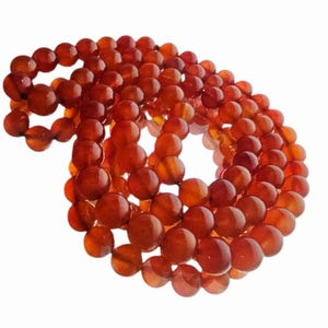May include: A necklace composed of numerous round, polished beads in shades of orange and red. The beads are strung together, forming a long, looping strand. The necklace is displayed against a white background.