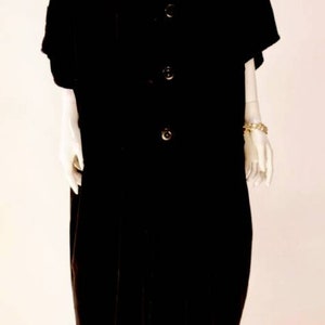 Puede incluir: Un vestido de terciopelo negro con botones en la parte delantera y mangas cortas. El vestido est&aacute; en un maniqu&iacute; blanco.