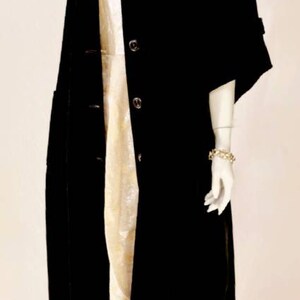 Puede incluir: Un abrigo de terciopelo negro con cuello alto y tres botones. El abrigo tiene mangas cortas y un corte holgado. El maniqu&iacute; lleva un collar de oro y una diadema de oro.