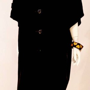 Puede incluir: Una chaqueta negra de manga larga con botones y una bufanda a cuadros blancos y morados. La chaqueta tiene cuello y la lleva un maniqu&iacute; con cabeza y brazos blancos.