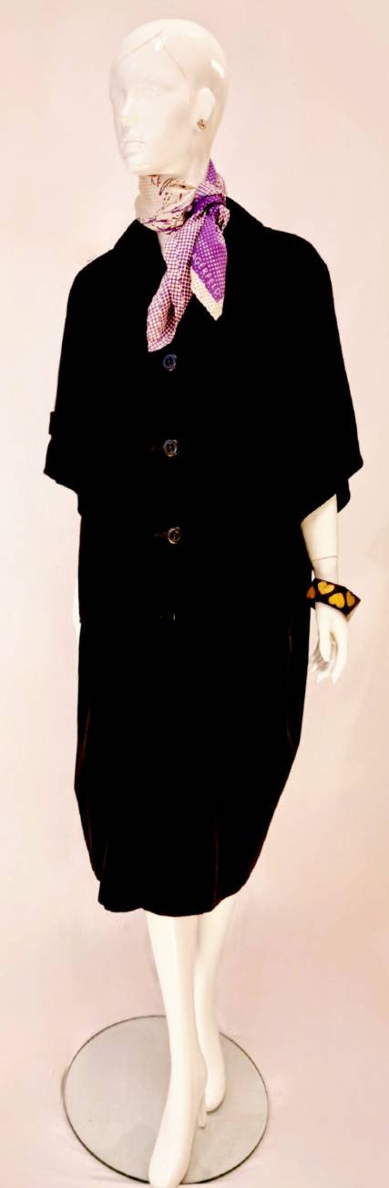 Puede incluir: Una chaqueta negra de manga larga con botones y una bufanda a cuadros blancos y morados. La chaqueta tiene cuello y la lleva un maniqu&iacute; con cabeza y brazos blancos.