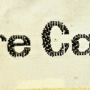 Puede incluir: Etiqueta de tela blanca con texto bordado en negro que dice "Pierre Cardin PARIS".