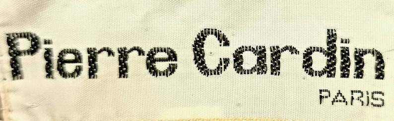 Puede incluir: Etiqueta de tela blanca con texto bordado en negro que dice "Pierre Cardin PARIS".