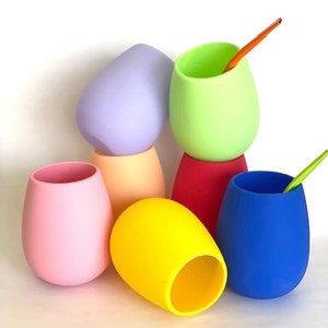 Peut inclure: Six gobelets en silicone de différentes couleurs, dont rose, jaune, bleu, vert et violet. Les gobelets sont empilés les uns sur les autres, avec une paille qui sort du gobelet du haut.