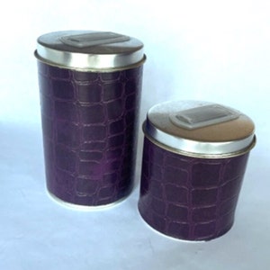 May include: Two purple metal canisters with silver lids. The canisters have a crocodile skin pattern.