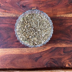 May include: A clear glass bowl filled with dried green yerba mate leaves.