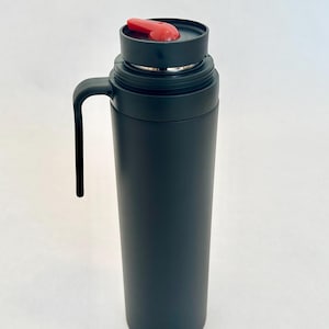May include: A black stainless steel travel mug with a black handle and a red lid. The mug has a sleek, modern design.