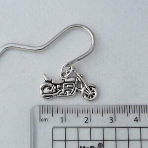 May include: Silver motorcycle charm earring with a hook fastening. The charm is approximately 1.5 inches long and is shown next to a ruler.