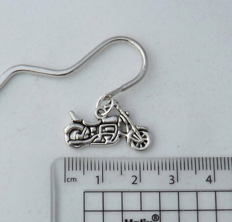 May include: Silver motorcycle charm earring with a hook fastening. The charm is approximately 1.5 inches long and is shown next to a ruler.