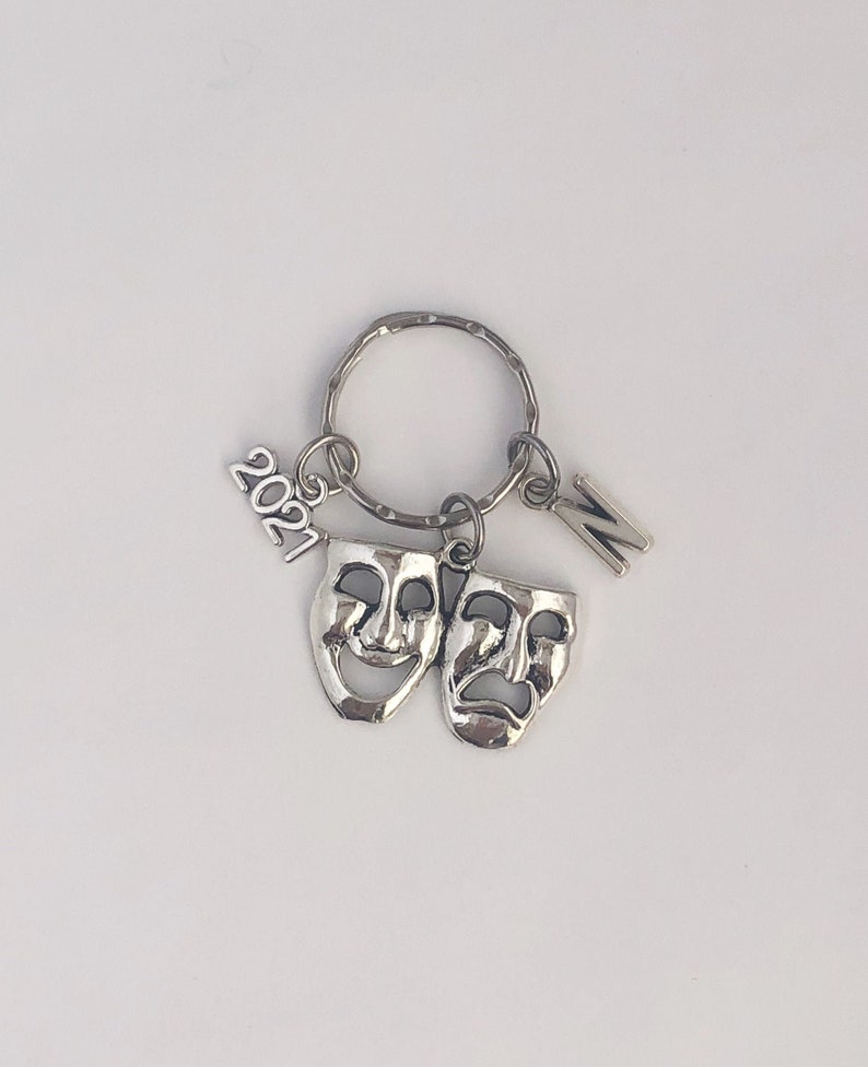 May include: Silver keychain with a 2021 charm, a letter N charm, and two silver masks, one smiling and one frowning.