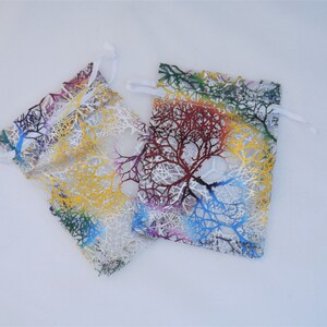 May include: Two small, white, mesh drawstring bags with colorful tree branch designs. The bags are made of a sheer fabric with a white background and colorful tree branches printed on them. The bags are lying flat on a white surface.