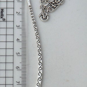 May include: Silver bookmark featuring a detailed motorcycle design. The bookmark is 9 cm long and has a decorative swirl pattern.