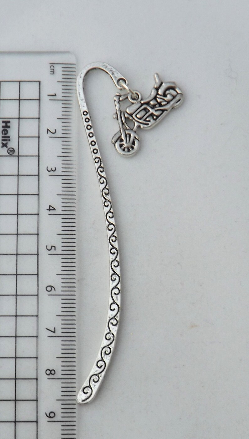 May include: Silver bookmark featuring a detailed motorcycle design. The bookmark is 9 cm long and has a decorative swirl pattern.