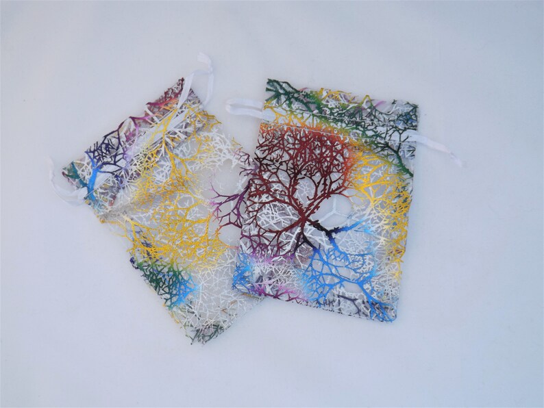 May include: Two small, white, mesh drawstring bags with colourful tree branch designs. The bags are made of sheer fabric with a white drawstring.