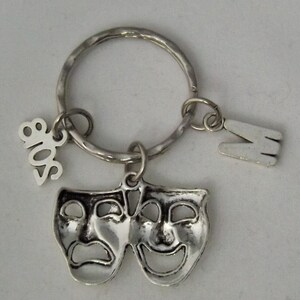 May include: Silver key chain with a pair of theater masks, a charm with the year 2018, and a charm with the letter M.