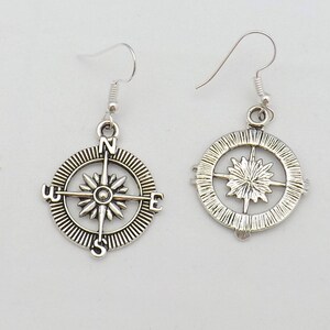 May include: A pair of silver compass earrings with a starburst design in the center. The earrings are on a white background.