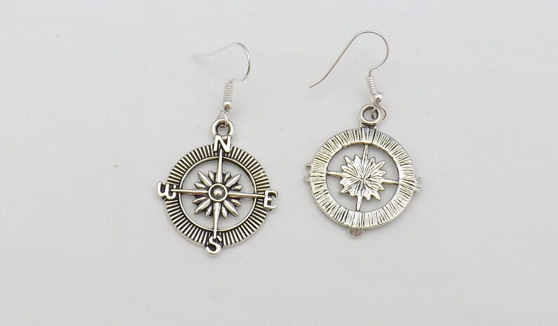 May include: A pair of silver compass earrings with a starburst design in the center. The earrings are on a white background.