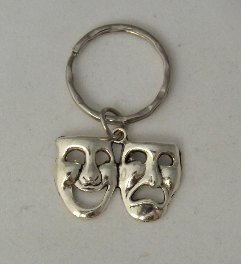 May include: Silver-toned key chain with a pair of theatrical masks. The masks are attached to a silver-toned key ring. One mask is smiling and the other is frowning.