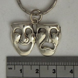 May include: Silver-toned key chain featuring a pair of theatrical masks, one smiling and one frowning. The masks are approximately 1 inch in size.
