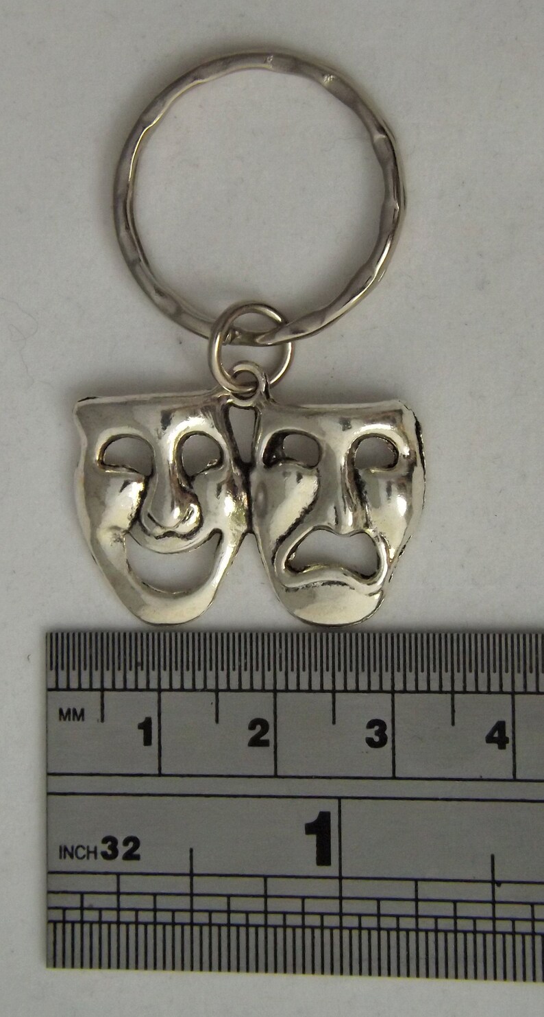 May include: Silver-toned key chain featuring a pair of theatrical masks, one smiling and one frowning. The masks are approximately 1 inch in size.