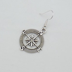 May include: Silver compass earring with a star design and the letters N, S, E, and W.