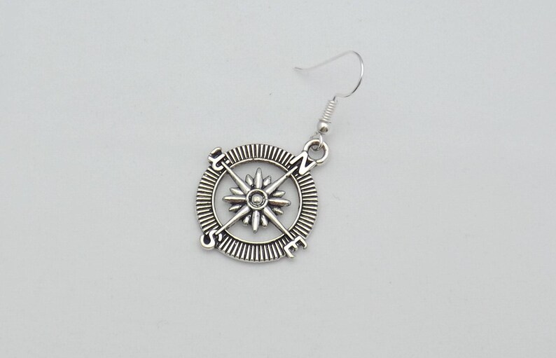 May include: Silver compass earring with a star design and the letters N, S, E, and W.
