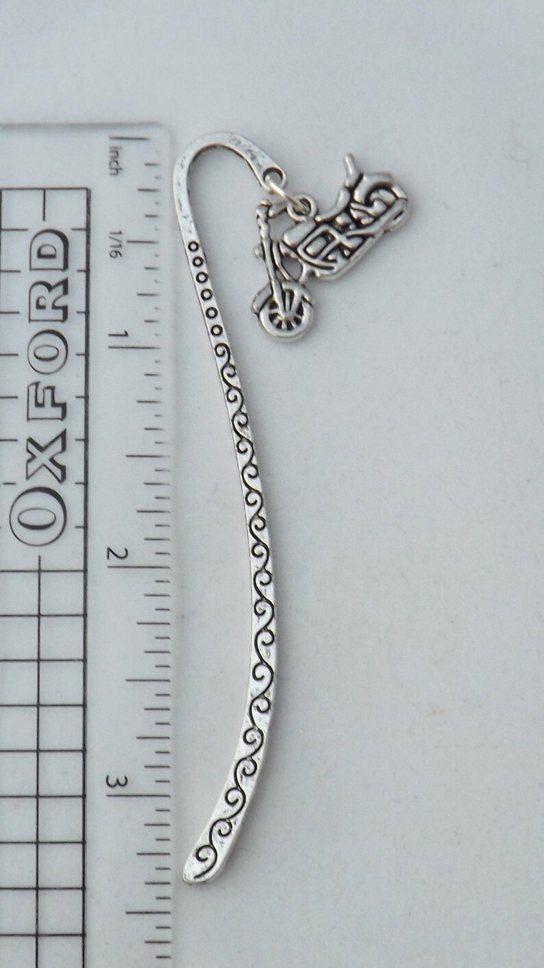 May include: Silver bookmark with a motorcycle charm. The bookmark is approximately 7.6 cm long and features a decorative design along the edge.
