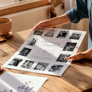May include: A personalized 1st Anniversary calendar print featuring black and white photos. The calendar is dated October 2026, with a heart marking a date. The print is held by a person, displayed on a wooden surface.