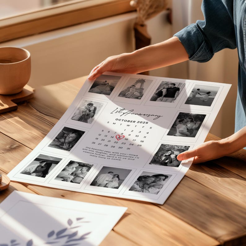 May include: A personalized 1st Anniversary calendar print featuring black and white photos. The calendar is dated October 2026, with a heart marking a date. The print is held by a person, displayed on a wooden surface.