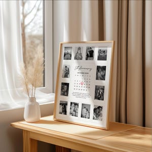 May include: A framed photo collage with a light wood frame. The collage features multiple black and white photos and a calendar with the text "1st Anniversary October 2025". The frame is displayed on a wooden table near a window.