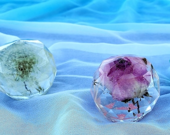 May include: Three clear glass spheres with different flower arrangements inside. The spheres are faceted and have a geometric shape. The flowers are a dandelion, a rose, and a green flower.