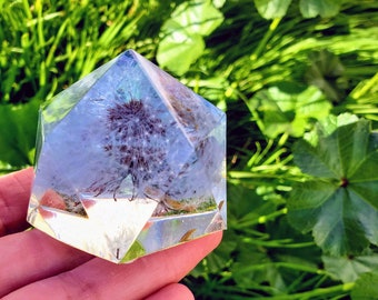 May include: A clear glass pyramid with a dried flower inside. The pyramid is sitting on a hand.