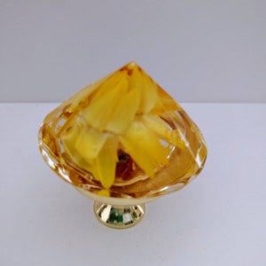 May include: A gold-toned cabinet knob with a clear glass top that has a yellow flower design inside.