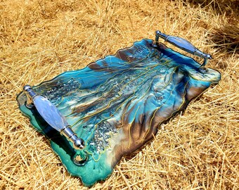May include: A teal and brown resin serving tray with gold accents and two silver handles. The tray has a unique, abstract design.