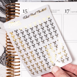 May include: A sheet of gold and black bow stickers with the text "Failed Heart Checklist" and "Adore Planning" on the sheet.