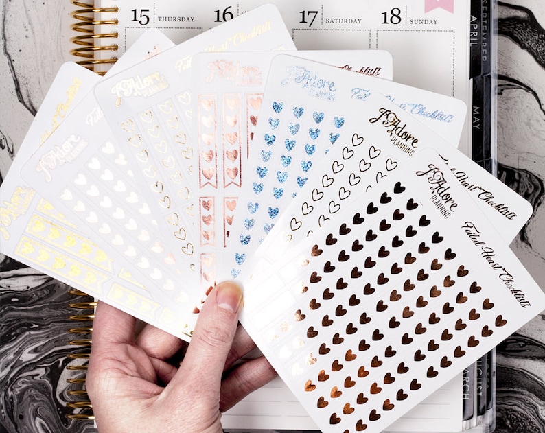 May include: A set of planner stickers with a heart theme. The stickers are in various colors, including gold, rose gold, and blue. The stickers feature different designs, including hearts, banners, and the text "I Adore Planning".
