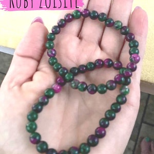 Może przedstawiać: Dwa zielone i fioletowe bransoletki z kamieni szlachetnych z okrągłymi koralikami. Bransoletki są wykonane z rubinowego zoisitu.