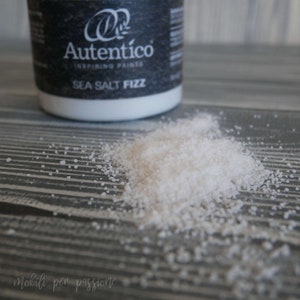May include: A white jar of sea salt fizz paint with the text "Autentico Inspiring Paints" and "Sea Salt Fizz" on the label. A pile of white sea salt is spilled on a gray wooden surface.