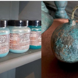 May include: A close-up of a shelf with several jars of  "Autentico Inspiring Paints" in the colors Aged Copper and Aged Green. The jars are arranged in a row on a shelf. A round, copper-colored ornament with a green patina is shown on the right side of the image.