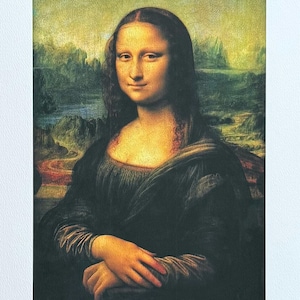 May include: A print of the Mona Lisa, a famous Renaissance portrait. The subject is a woman with a subtle smile, wearing a dark dress. The background features a landscape with muted green and yellow tones. The artwork is framed in white.